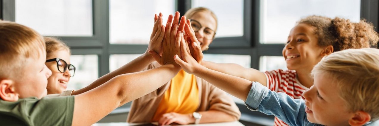 Schulsozialarbeit Lehrer sitzt mit Schülern an einem Tisch, freuen sich und klatschen ab